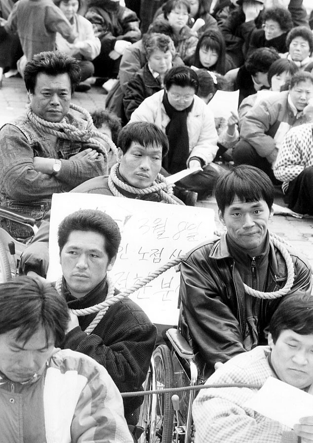 1995년 최정환 열사의 분신자살 이후 ‘장애인 노점상 최정환씨 분신사건 비상대책위’ 소속 회원과 대학생 300여명이 서초구청 앞에서 시위를 벌이고 있다. 이들은 밧줄로 서로의 목을 감고 ‘폭력단속반 해체’와 ‘관련자 처벌’을 요구했다. 최정환씨가 남긴 유언은 이후 장애해방 투쟁의 중대한 불씨 역할을 하게 된다. <한겨레> 자료사진