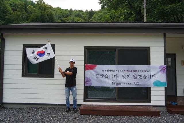 션이 새롭게 완성된 A씨의 보금자리 앞에서 태극기를 흔들고 있다. 한국해비타트 제공