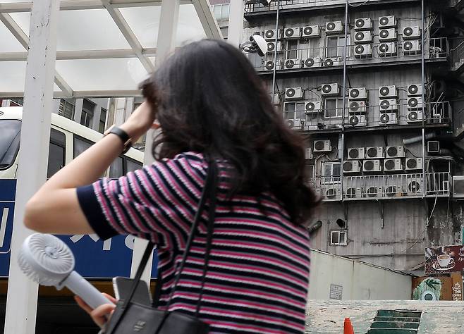 전국에 때이른 폭염이 지속되는 가운데 지난 4일 서울 시내 한 건물 외벽에 가득 매달린 에어컨 실외기 앞으로 한 시민이 휴대용선풍기로 더위를 식히며 지나가고 있다. /뉴스1