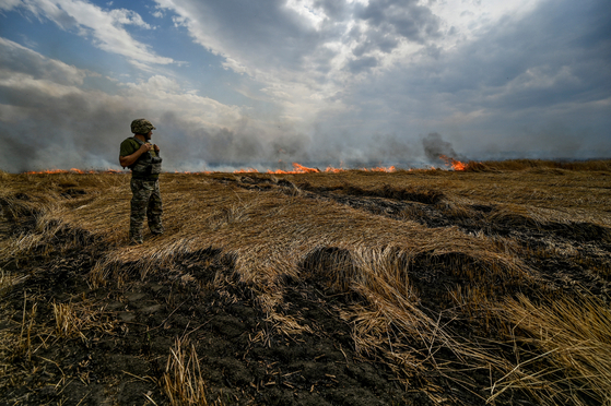 지난달 17일(현지시간) 우크라이나 남동부 자포리자와 도네츠크 접경 지역에서 한 우크라이나 병사가 러시아군의 집중 폭격에 불타고 있는 밀밭을 바라보고 있다. [로이터=연합뉴스]