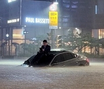 지난 8일 밤 서울의 한 도로가 물에 잠기자 시민이 차체 위로 올라와 있다. 뉴스1