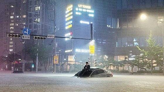 지난 8일 서울 서초동 아파트 단지 앞에서 한 남성이 침수된 차량 위로 올라가 몸을 피하고 있다. 사진 온라인 커뮤니티 캡처