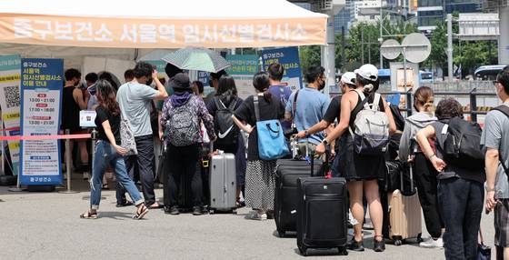 People with luggage wait to get tested for Covid-19 at a testing center erected outside Seoul Station in central Seoul on Sunday. [YONHAP]