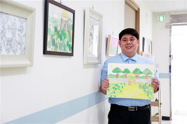 발달장애인 김민영씨가 서울 구로장애인가족지원센터에서 자신의 그림을 든 채 웃고 있다. 김씨가 그린 그림들은 구로구청 내에 전시돼 있다.구로구 제공