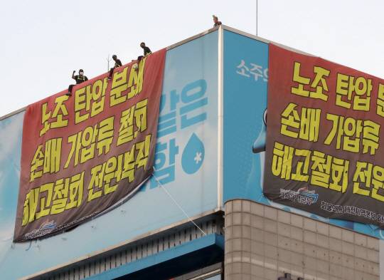 지난 16일부터 하이트진로 본사 옥상에서 고공농성을 하고 있는 민주노총 화물연대 조합원들이 18일 오후 서울 강남구 하이트진로 본사 앞에서 열린 ‘고공농성 투쟁 승리 결의대회’를 지켜보고 있다. 뉴시스