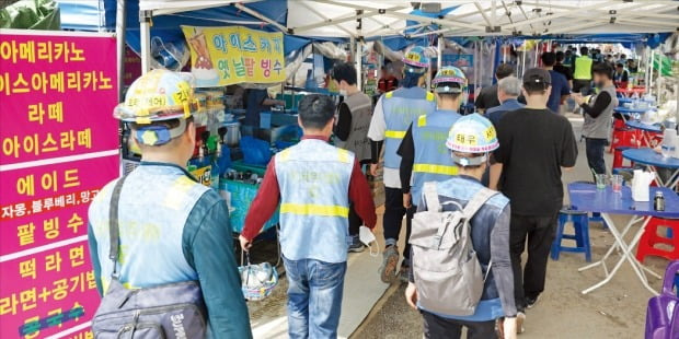 < 붐비는 함바집 > 삼성전자 경기 평택 반도체 공장 현장에서 일하는 일용직 노동자들이 23일 점심 식사를 하기 위해 도로변에 늘어선 노점 앞을 지나가고 있다. 사업장 인근엔 수백 개의 함바집(간이식당)과 노점 등이 성업 중이다. /평택=허문찬  기자