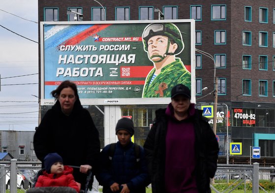 지난 20일 러시아 상트페테르부르크의 러시아 군인 모집 광고판 아래에서 러시아인들이 걸어가고 있다. AFP=연합뉴스