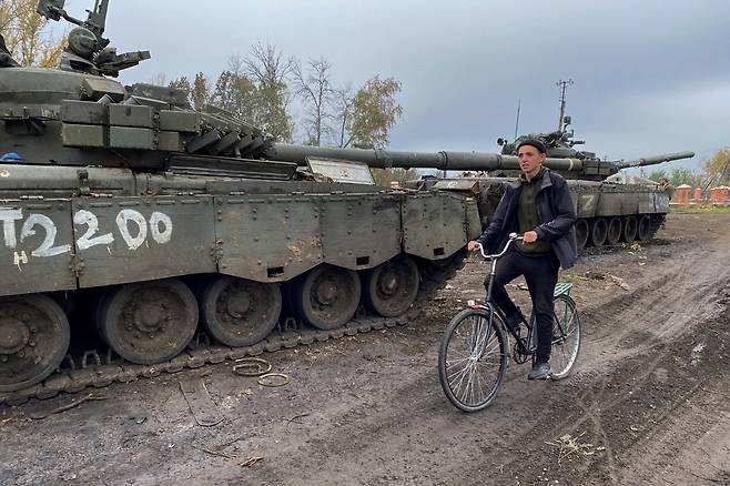 우쿠라이나 안에 세워진 러시아 탱크의 옆을 지나는 주민의 모습.[로이터]