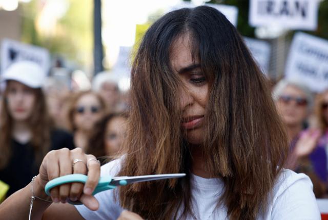 지난 6일 스페인 시민이 마드리드에 위치한 이란 대사관 앞에서 열린 마흐사 아미니(향년 22세) 추모 및 이란 폭정 규탄 시위에서 머리카락을 가위로 자르고 있다. 지난달 16일 아미니가 히잡을 제대로 착용하지 않았다는 이유로 이란 종교경찰에 체포된 뒤 사망하자 이란을 비롯한 전 세계에서 '히잡 의문사'에 항의하는 시위가 잇따르고 있다. 로이터=연합뉴스