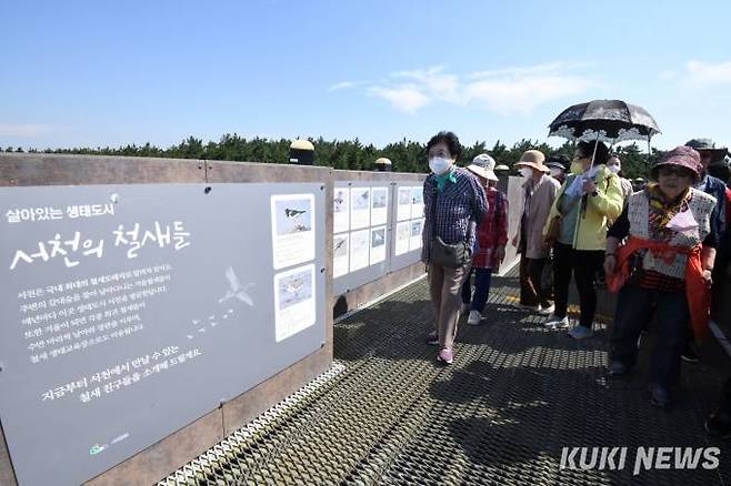서천군 장항스카이웨이를 찾은 관광객들이 전망테크 앞에 전시된 서천의 갯벌에 날아드는 철새들 사진을 살펴보고 있다.