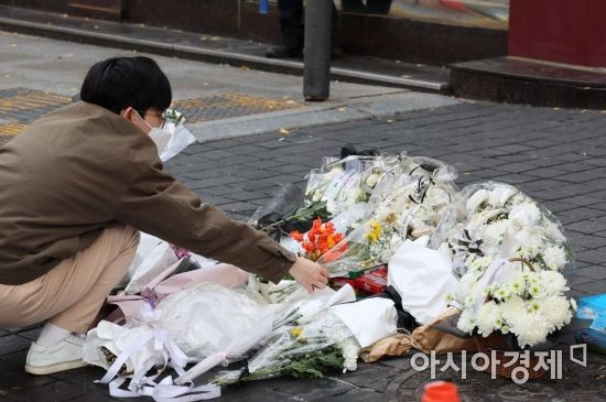 13일 서울 용산구 이태원 참사 현장 앞 인도에서 한 자원봉사자가 시민들이 두고 간 국화꽃과 추모 메세지를 정리하고 있다./윤동주 기자 doso7@