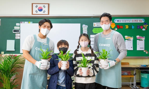 코웨이 임직원 봉사자와 초등학생들이 청정학교 교실숲 식물을 들고 포즈를 취하고 있다. 사진=코웨이 제공