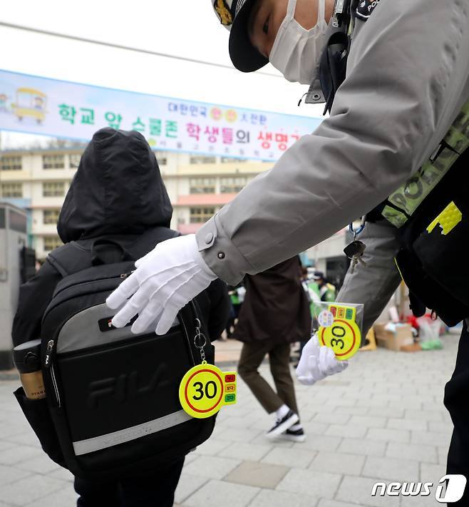 22일 서울 서대문구 고은초 앞에서 열린 교통안전캠페인에 참가한 경찰관이 등굣길에 나선 한 어린이의 가방에 교통안전 고리를 달아주고 있다. 2022.11.22/뉴스1 ⓒ News1 장수영 기자