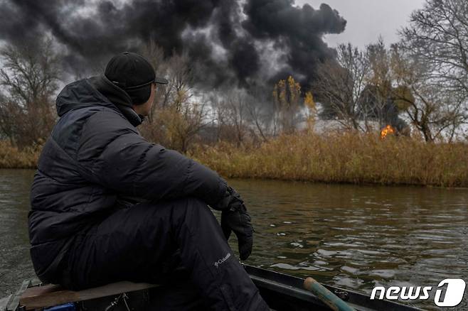 20일(현지시간) 우크라이나가 최근 탈환한 헤르손의 검은 연기가 솟아오르는 유류 저장소를 드니프로 강에서 보트를 탄 어부가 바라 보고 있다. ⓒ AFP=뉴스1 ⓒ News1 우동명 기자