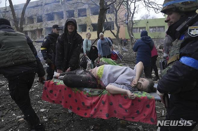 [마리우폴=AP/뉴시스] 3월9일(현지시간) 우크라이나 마리우폴에서 산부인과 병원이 러시아군의 포격을 받아 응급 구조요원과 자원봉사자들이 부상한 임신부를 옮기고 있다. 볼로디미르 젤렌스키 우크라이나 대통령은 "아이들과 사람들이 병원 잔해에 깔려 있다"라며 이번 공격을 "잔혹 행위"라고 비난했다. 2022.03.10.