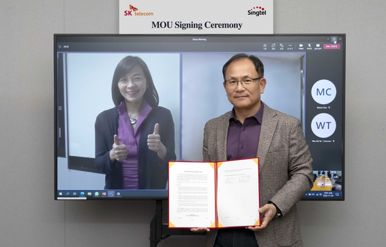 Anna Yip, on screen, Singtel's consumer CEO, and Ha Min-yong, SK Telecom chief development officer, pose for a photo during a signing ceremony held Monday. [SK TELECOM]