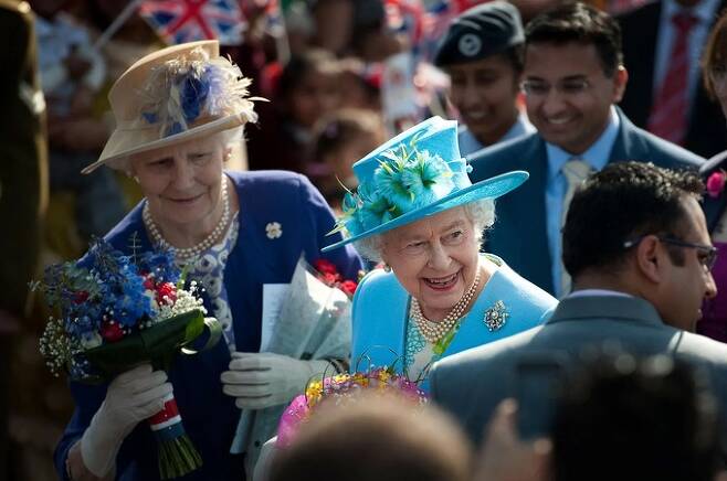 엘리제베스 2세 영국 여왕이 생전인 2012년 런던의 한 학교를 방문했을 때 사람들이 건네준 꽃다발을 시녀가 챙기고 있다. 런던=AFP연합뉴스