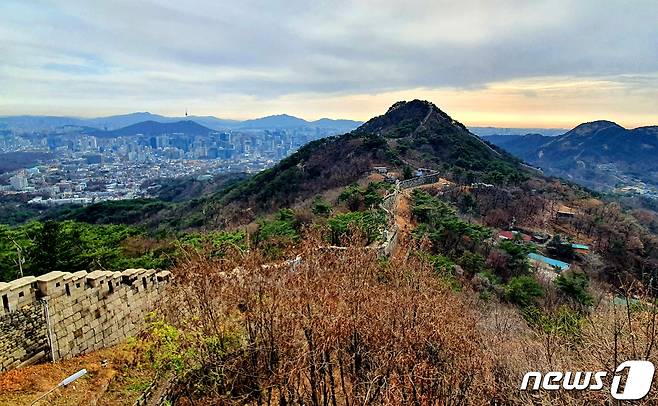 곡장에서 바라본 풍경. 가운데 백악산 정상에서 뻗어내린 성곽이 용의 지느러미처럼 다가서는 가운데, 남산 뒤로 청계산과 관악산이 불룩하고, 오른쪽 인왕산 뒤로 서해바다 위 하늘이 노랗게 물들고 있다.