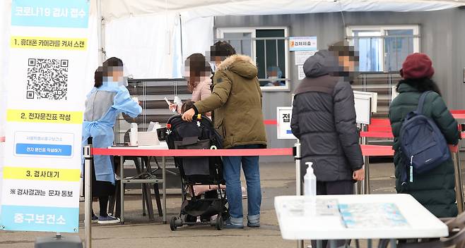 People stand in line at a COVID-19 screening center by Seoul Station on Sunday. (Yonhap)