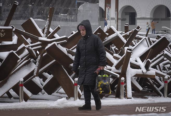 [키이우=AP/뉴시스] 12일(현지시간) 우크라이나 키이우에서 한 여성이 눈 내린 대전차 장애물 옆을 지나가고 있다. 2022.12.13.