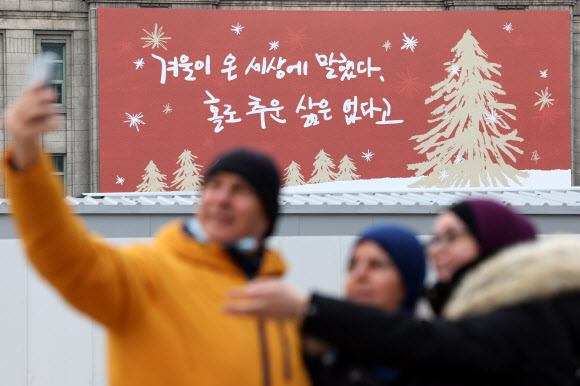 서울꿈새김판 앞에서… - 관광객들이 12일 오전 서울 중구 서울도서관 외벽에 새단장한 서울꿈새김판 앞에서 기념사진을 찍고 있다. 시는 시민 공모로 선정한 겨울편 문안 ‘겨울이 온 세상에 말했다. 홀로 추운 삶은 없다고’를 게시했다.뉴시스