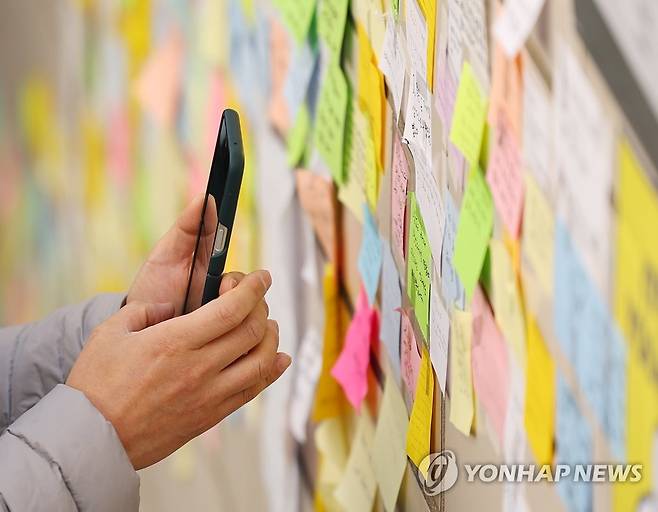 '기억할게' (서울=연합뉴스) 김도훈 기자 = 6일 오후 서울 용산구 이태원역 1번 출구에서 한 시민이 추모객들의 메시지를 휴대전화로 촬영하고 있다. 2022.11.6 superdoo82@yna.co.kr