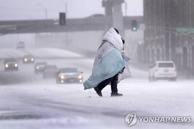 미국 세인트루이스에서 눈이 내리는 가운데 담요를 두르고 길을 건너는 한 시민 [세인트루이스 AP=연합뉴스]