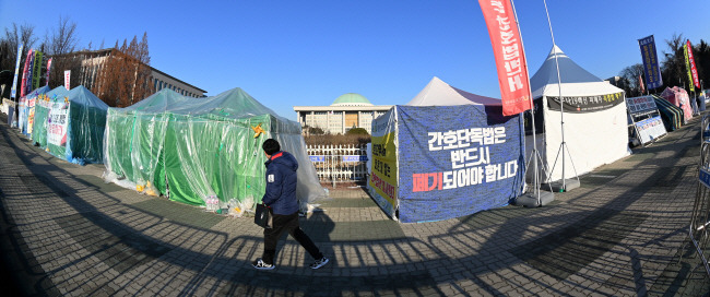 “인도인지, 캠핑장인지…”　   : 4일 오전 한 시민이 서울 영등포구 국회의사당 앞 인도에 설치된 민주노총 등 각종 단체의 불법 천막 앞을 지나가고 있다. 천막·텐트의 난립으로 10m 이상 넉넉한 폭의 인도가 절반으로 줄어들어 여의도 직장인 등이 큰 불편을 겪고 있다.  문호남 기자