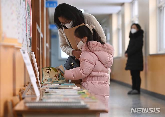 [수원=뉴시스] 김종택 기자 = 초등학교 예비소집일인 지난해 12월26일 오후 경기도 수원시 장안구 송원초등학교에서 입학을 앞둔 어린이가 엄마와 함께 교과서를 살펴보고 있다. 2023.01.07. jtk@newsis.com