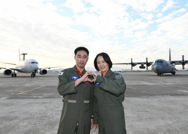 공군 최초 비행대대장 부부인 김익규(왼쪽), 김민지(오른쪽) 중령이 각각 대대장으로서 지휘하는 E-737 항공통제기(왼쪽)와 C-130 수송기(오른쪽)를 배경으로 하트를 만들어 보이고 있다. [사진제공=공군]