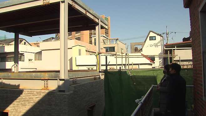 마을 주민이 자신의 집 2층 베란다에서 건축이 중단된 사원을 바라보고 있다.