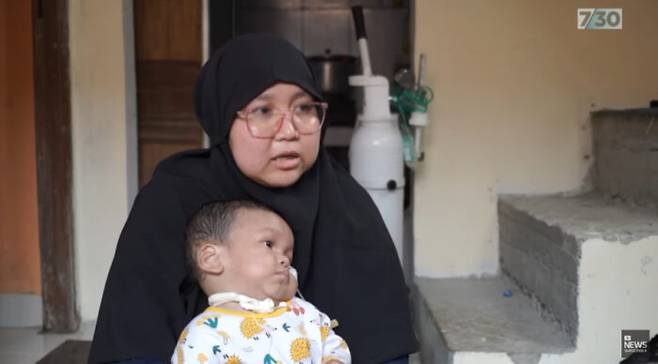 인도네시아의 한 여성이 감기 시럽 복용 후 신장 건강에 문제가 생긴 자녀를 안고 아이의 건강 상태에 대해 이야기하고 있다. [사진=ABC 뉴스 유튜브]