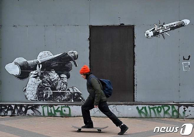25일(현지시간) 러시아 침공 속 우크라이나 키이우에서 병사가 휴대용 대전차 미사일을 발사하는 모습을 그린 벽화 앞에 소년에 스케이트 보드를 타고 있다. ⓒ AFP=뉴스1 ⓒ News1 우동명 기자