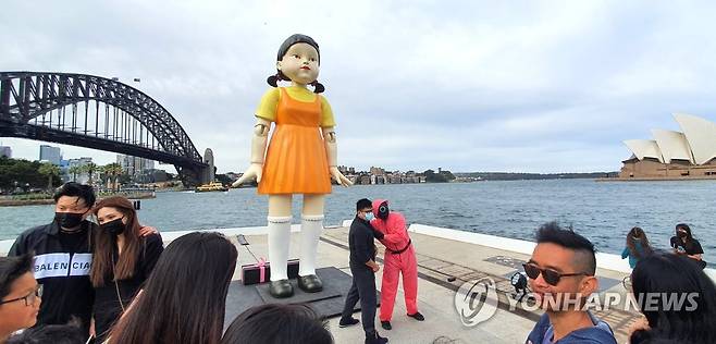 호주 시드니에 등장한 오징어게임 '영희' 인형 (시드니=연합뉴스) 정동철 통신원 = 호주 넷플릭스가 2021년 10월 29일부터 11월 1일까지 4일간 시드니의 명소 오페라 하우스와 하버 브리지 사이에 '무궁화꽃이 피었습니다' 게임의 술래 '영희' 인형과 분홍색 제복의 진행 요원 등 '오징어 게임' 체험장을 설치해 현지인들의 뜨거운 호응을 받았다. 
    나흘간 1만 명 가량의 인파가 체험장을 찾아 호주에서의 '오징어 게임' 인기를 실감할 수 있었다. 
    사진은 1일 호주 시드니하버에 설치된 영희 인형을 찾은 시민들의 모습. 2021.11.1 dcj@yna.co.kr