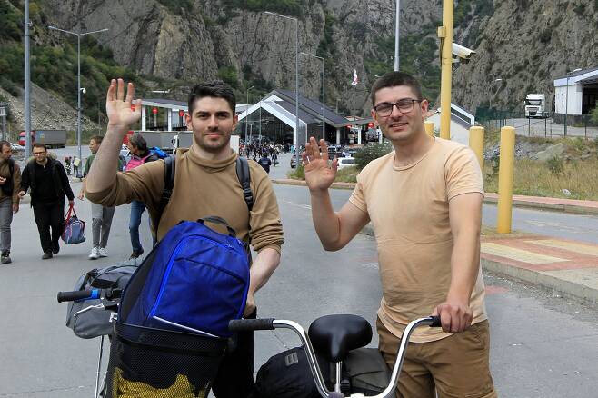 지난 28일 자전거를 타고 조지아로 입국한 두 명의 러시아인이 취재진을 향해 손을 흔들고 있다. AP=연합뉴스