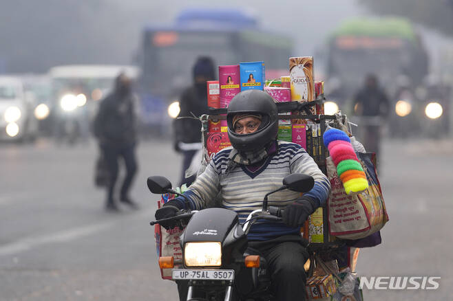[뉴델리=AP/뉴시스] 27일(현지시간) 인도 뉴델리에서 오토바이로 물건을 파는 한 상인이 춥고 안개가 낀 아침 일터로 향하고 있다. 인도 북부 대부분 지역을 덮친 한파에 더해 짙은 안개가 태양 빛을 차단해 낮에도 추운 날씨가 이어지면서 철도, 도로, 항공 운송에 차질이 빚어지고 있다. 2022.12.27.