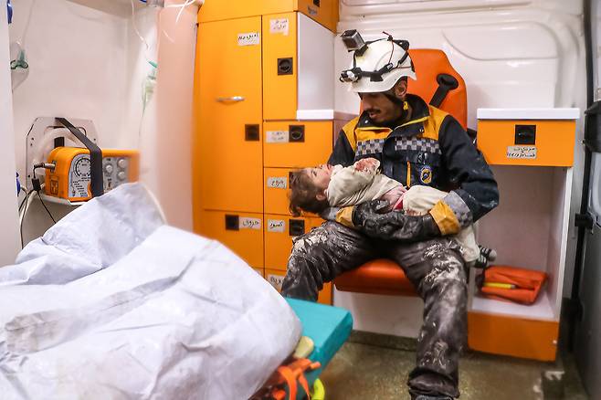 지난 6일 시리아 이들리브의 건물 잔해 속에서 구해낸 아이를 한 구조대원이 품에 안고 보고 있다. /UPI 연합뉴스