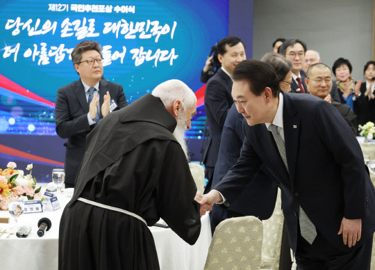 윤석열 대통령이 16일 서울 용산 대통령실 청사 자유홀에서 열린 국민추천 포상 수여식에서 42년간 한센인과 중증장애인에 헌신한 유의배 신부(국민훈장 모란장)와 인사하고 있다. 연합뉴스