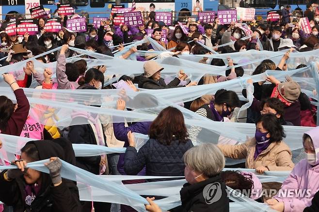 '유리천장을 깨부수자' (서울=연합뉴스) 세계여성의날을 나흘 앞둔 지난 4일 서울 종로구 보신각 앞에서 여성노동연대회의가 주최한 2023 여성노동자대회에서 참가자들이 여성차별의 상징인 유리천장을 깨고 나가자는 의미로 투명한 천을 찢는 퍼포먼스를 하고 있다.