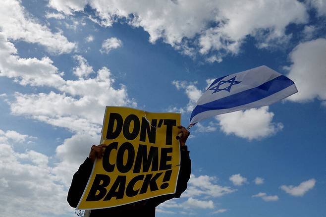 15일(현지시각) 이스라엘 벤구리온 공항이 위치한 로드에서 사법제도 개편에 반대하는 사람이 ‘돌아오지 마’라고 적힌 팻말과 이스라엘 국기를 들고 있다. 로드/로이터 연합뉴스