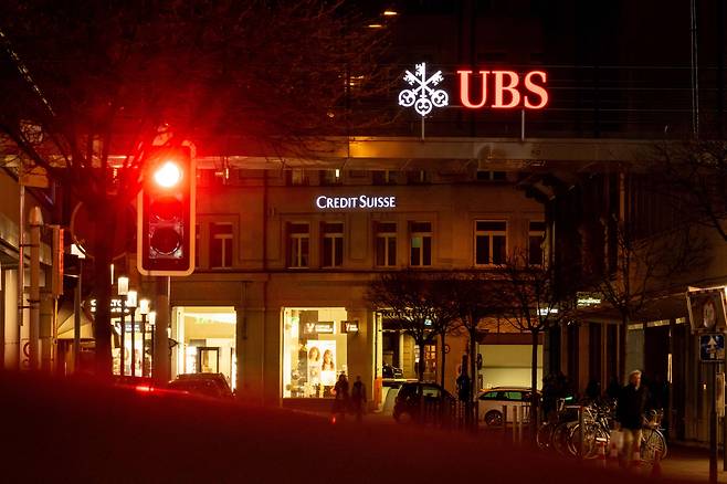 지난 18일(현지 시각) 스위스 취리히의 한 거리에 켜진 빨간 신호등 불빛 뒤로 스위스 은행 1위 UBS와 2위 크레디스위스의 간판이 보인다. 월스트리트저널 등에 따르면, UBS는 자금난에 빠진 크레디스위스 인수를 시도하고 있다. 성사될 경우 스위스 대형 은행 2곳을 합친 ‘공룡 은행’이 탄생하게 된다. UBS는 막대한 손실을 낸 크레디스위스의 투자은행 부문을 축소할 가능성이 큰 것으로 알려졌다./AFP·연합뉴스