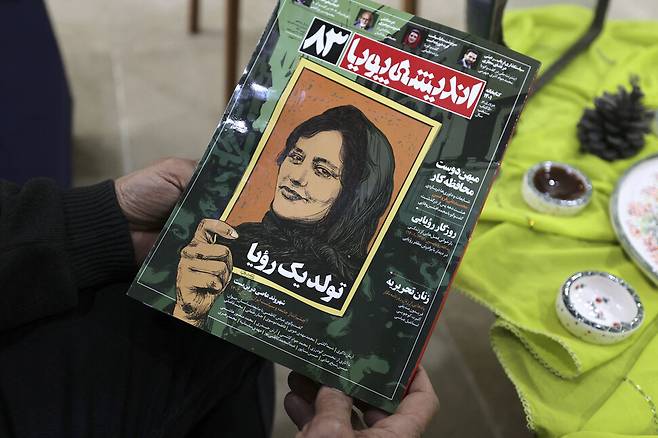 14일(현지시각) 이란 테헤란에서 한 시민이 마흐사 아미니의 얼굴이 그려진 이란 잡지를 들고 있다. 평범한 이란 여성이었던 아미니는 지난해 9월 히잡 착용 미비로 도덕경찰에 붙잡혔다 숨지면서 이란 전역에서 자유와 저항을 상징하는 인물이 됐다. 테헤란/AFP 연합뉴스
