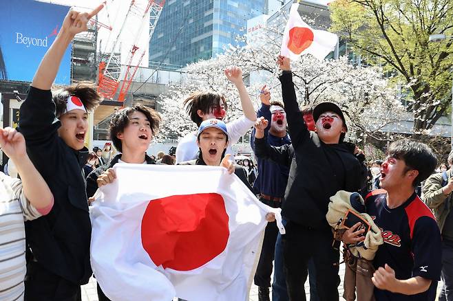 22일 도쿄 시부야역에서 야구 팬들이 일본 국기를 흔들면서 WBC에서 14년 만의 우승을 기뻐하고 있다. [AFP]