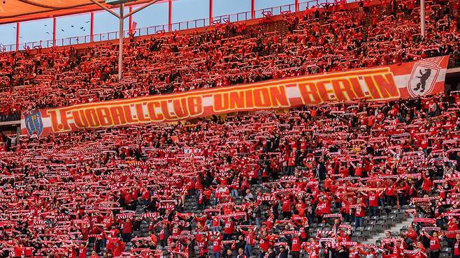 붉은 머플러를 펼치며 응원을 펼치는 우니온 베를린 팬들. 열성적인 팬들이 많은 분데스리가에서도 우니온 베를린 팬들은 특히 뜨거운 응원 열기로 유명하다. / 트위터