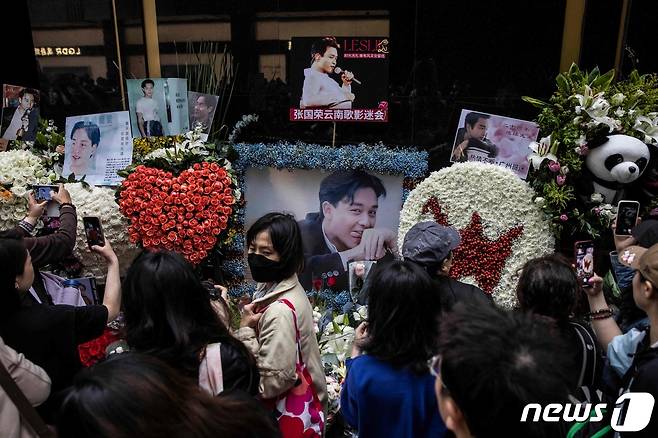 홍콩의 가수 겸 배우였던 장국영의 사망 20주기를 맞은 1일(현지시간) 홍콩에서 시민들이 길가에 놓인 추모 화환과 그의 생전 모습을 카메라에 담고 있다. 2023.04.01. ⓒ AFP=뉴스1 ⓒ News1 김성식 기자
