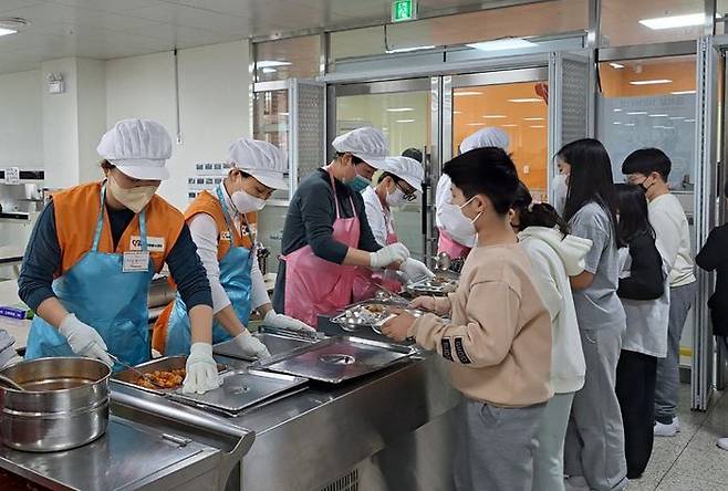 ⓒ과천시, 문원초 학교급식 인력난 해소 위해 자원봉사자 긴급 배치(주황색조끼를 입은 봉사자들이 학생들에게 배식하고 있다)