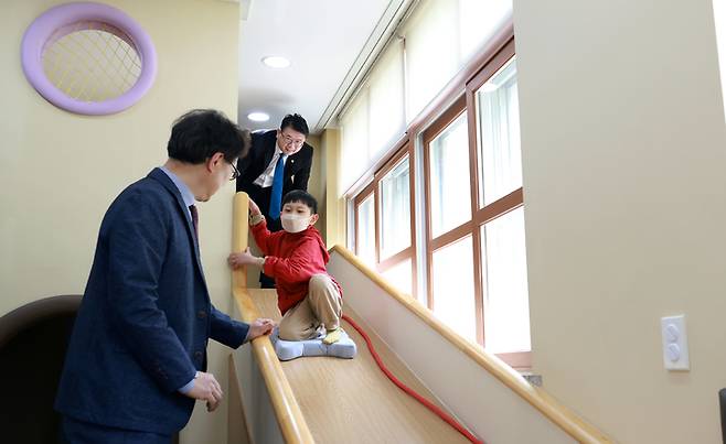 [대전=뉴시스] 지난 2일 대전 서구 원앙초등학교 1층 '금빛마을'에서 미끄럼틀을 타고 내려오는 한 학생. 뒤는 장상윤 교육부 차관. (사진=교육부 제공). 2023.05.08. photo@newsis.com *재판매 및 DB 금지
