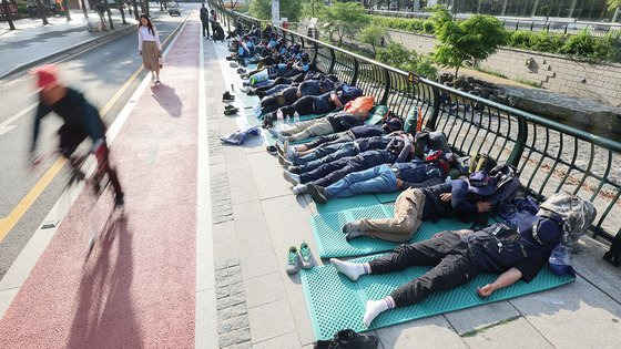 지난 17일 오전 출근시간대 시민들이 서울 중구 청계광장에서 전날 밤 총파업 결의대회 후 노숙하고 있는 민주노총 건설노조원들을 지나치고 있다. 연합뉴스