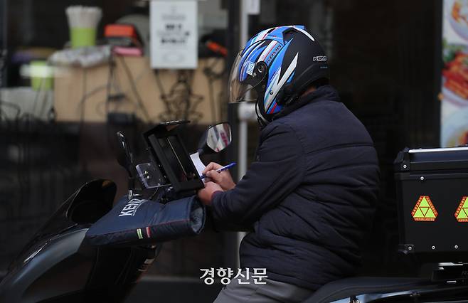 한 배달 노동자가 잠시 멈춰 서서 종이에 무언가 쓰고 있다. 한수빈 기자