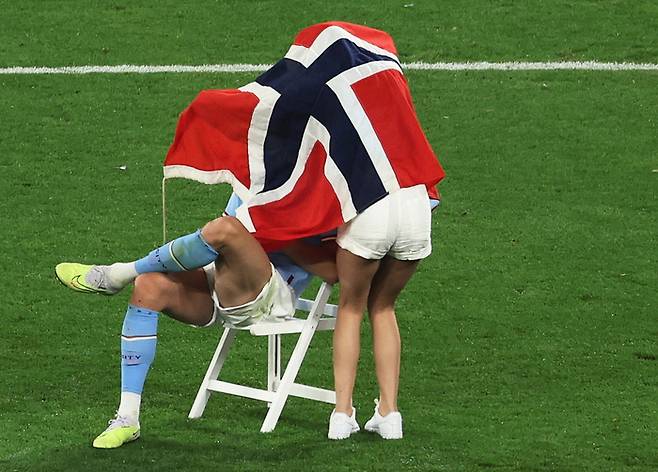맨체스터 시티 엘링 혼란이 11일 터키 이스탄불에서 열린 유럽축구연맹 채미언스리그에서 우승한 뒤 그라운드에 의자를 놓고 안자 있자 여자친구 아사벨 요한슨이 노르웨이 국기로 감싸고 있다. 로이터연합뉴스